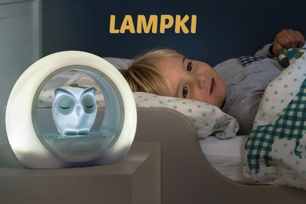 Dziecko leży w łóżku obok lampki nocnej w kształcie sowy.