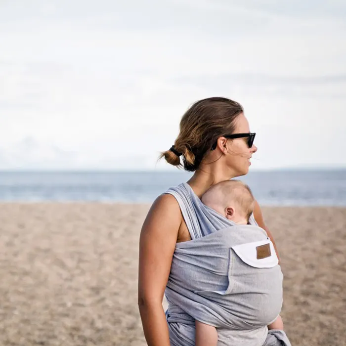 Mama z dzieckiem w chuście na brzuchu na plaży